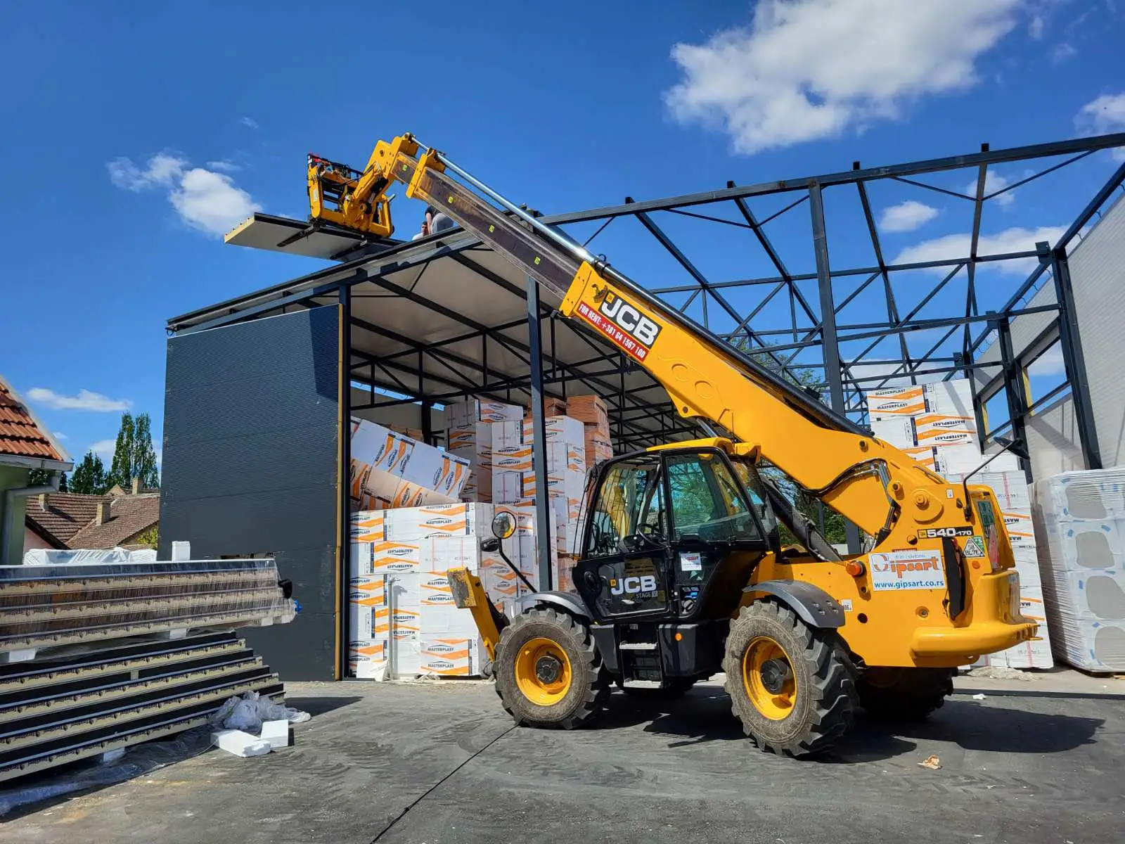 Telehandler lifting insulation panels into a steel-frame warehouse